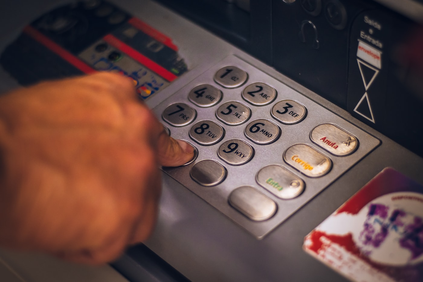 A hand entering a PIN at a cash machine keypad
